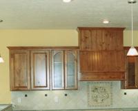 Thumb kitchen  traditional style  knotty alder  medium color  raised panel doors  tall half arch glass doors  angled wood hood with wainscot   6 standard crown  standard overlay